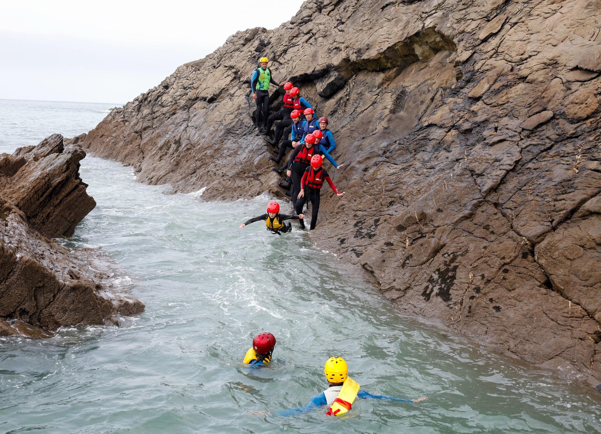 A group of people jumping into the water while coasteering in Cornwall